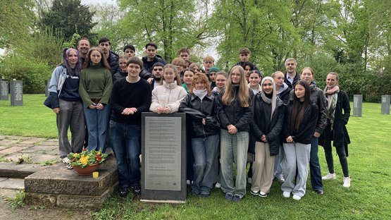 Ein Gruppe von Schülerinnen und Schülern steht hinter einer Informationstafel auf dem Friedhof Kassel-Bettenhausen.