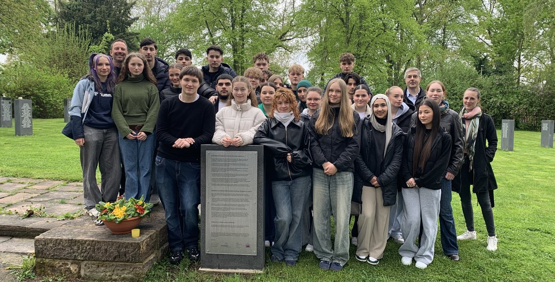 Ein Gruppe von Schülerinnen und Schülern steht hinter einer Informationstafel auf dem Friedhof Kassel-Bettenhausen.